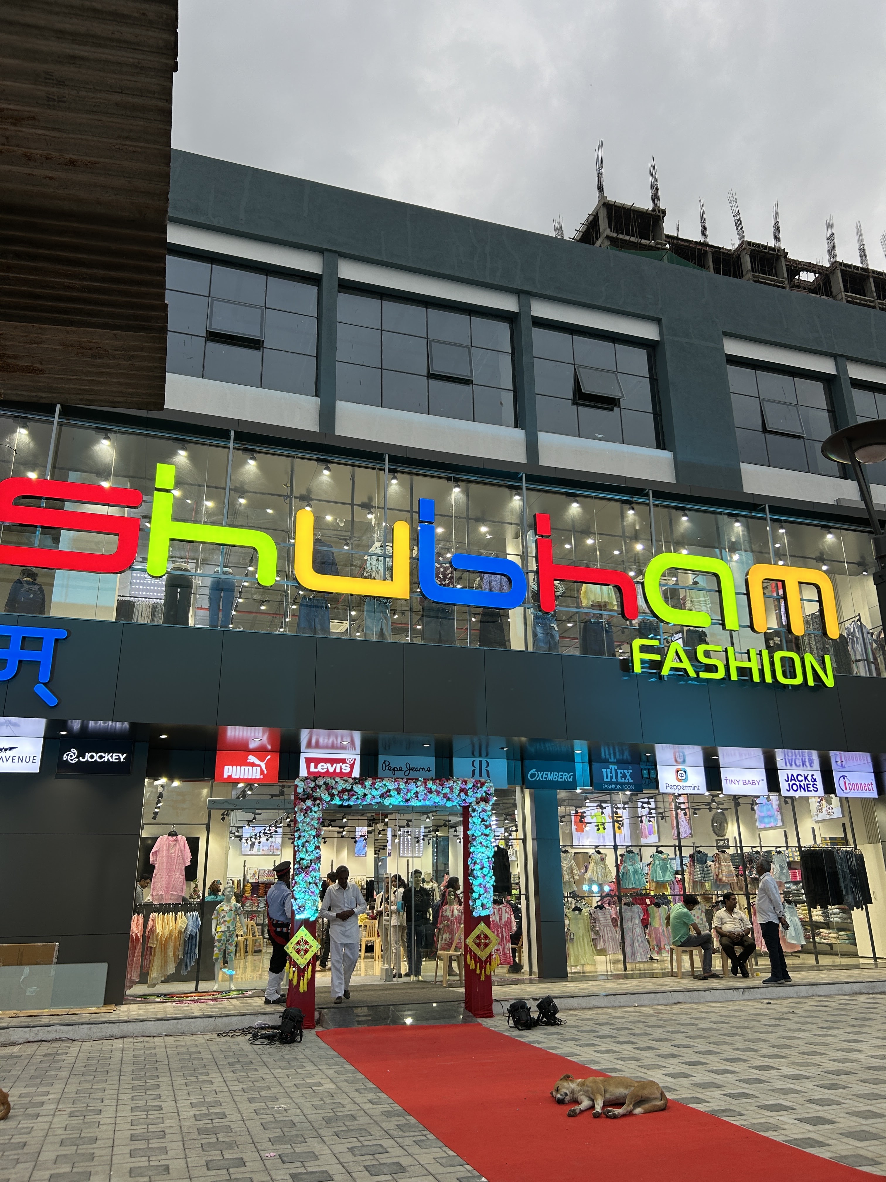 Shubham Fashion storefront during daytime at Montvert Kingstown, Pune, full building view with colorful signage, red carpet, and brand logos of Jockey, Puma, Levi's visible