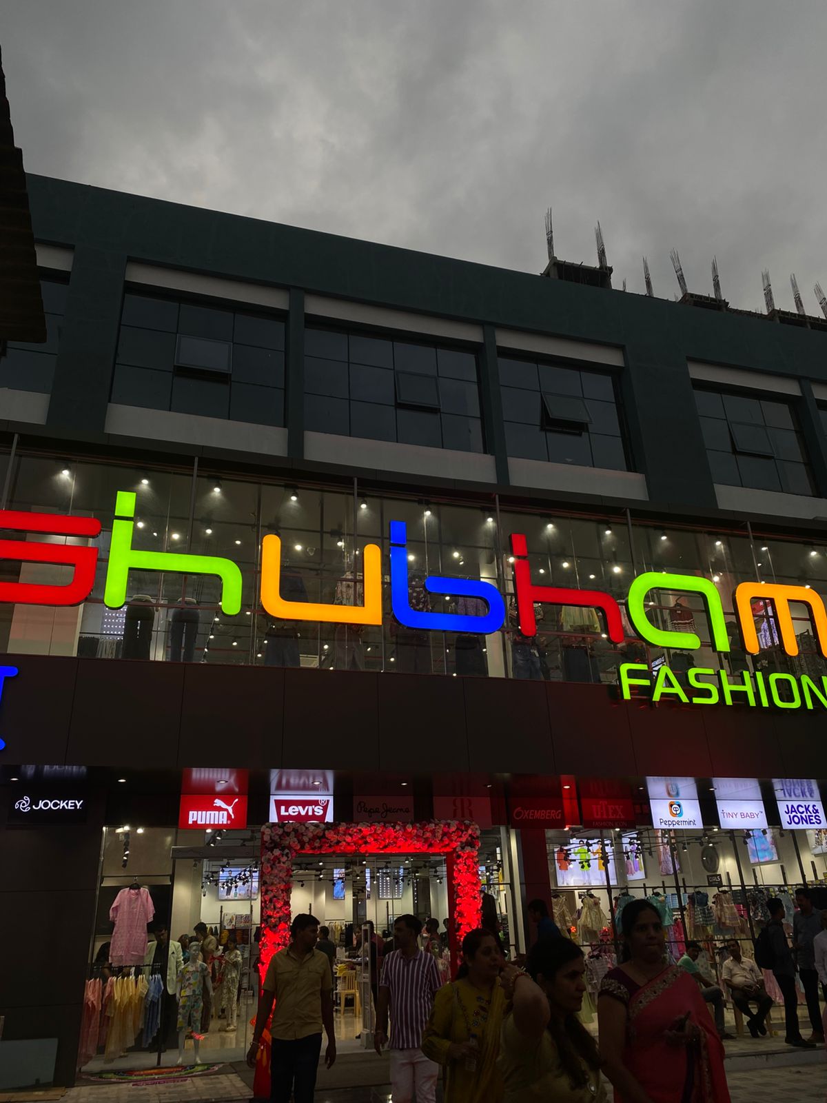 Shubham Fashion storefront at Montvert Kingstown, Pune. Illuminated signage at dusk with brand logos of Jockey, Puma, Levi's, Pepe Jeans, and Jack & Jones visible